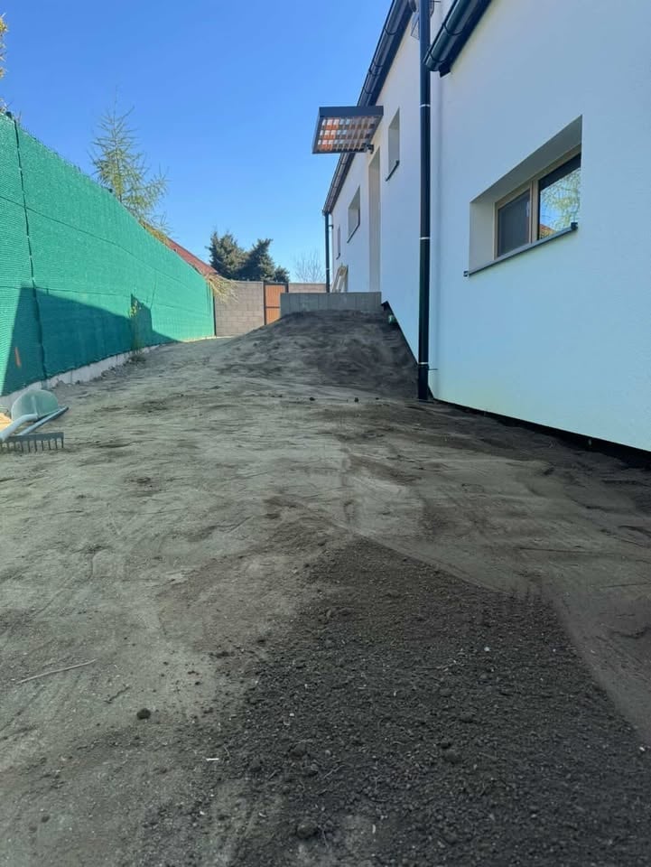 Modern house with white and dark exterior on a gravel driveway, with green construction fencing on the left side under clear blue sky