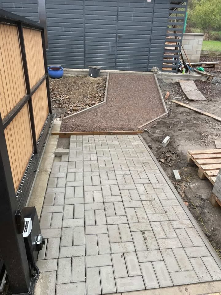 Newly laid paver patio beside a house with storage shed and garden area in background