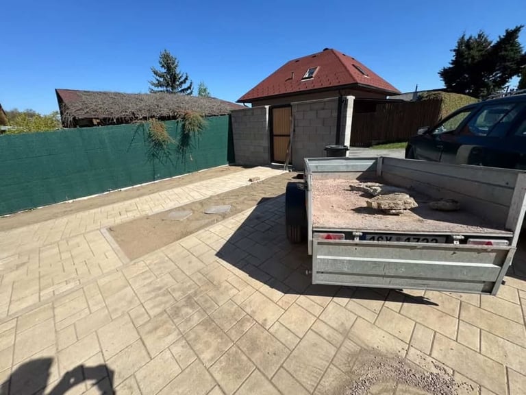 A paved driveway with a green fence, dome-roofed storage building, and trailer parked on the right side